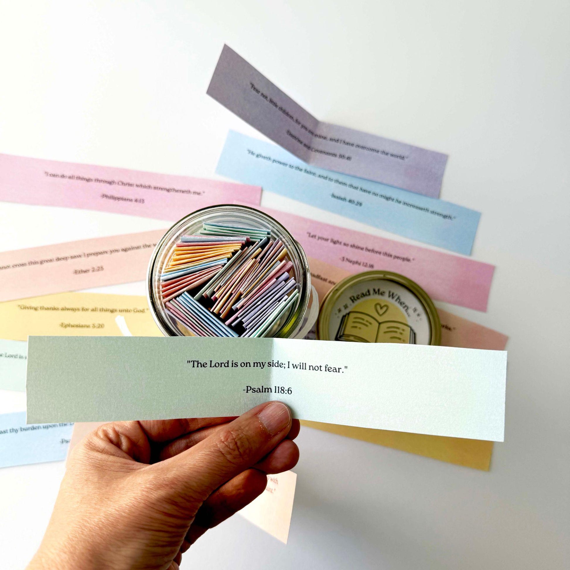 Hand holding a blue Read Me When scripture card beside open jar filled with colorful LDS encouragement verses