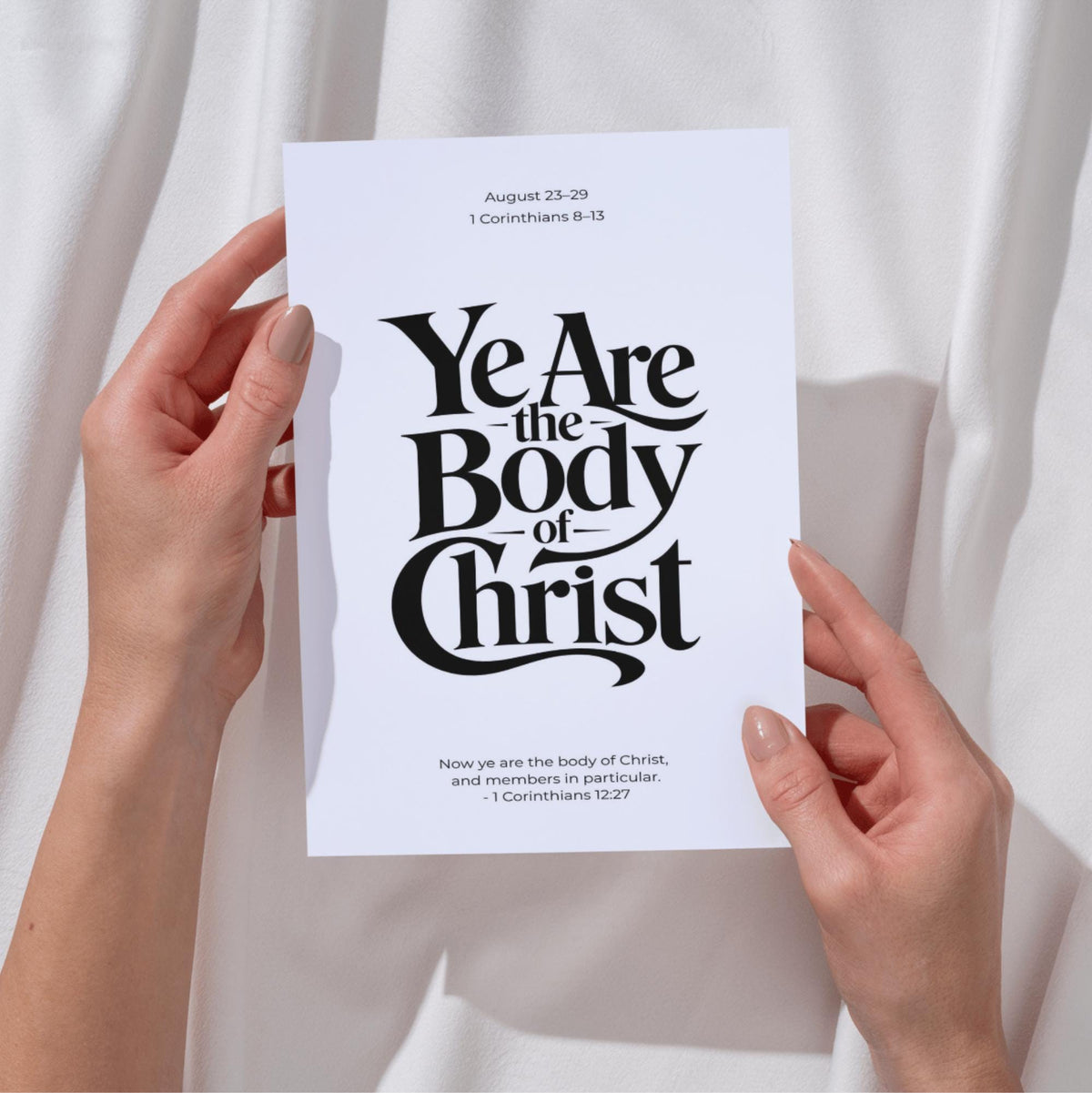 Person holding a Ye Are the Body of Christ black and white Bible verse typography poster, demonstrating the scale