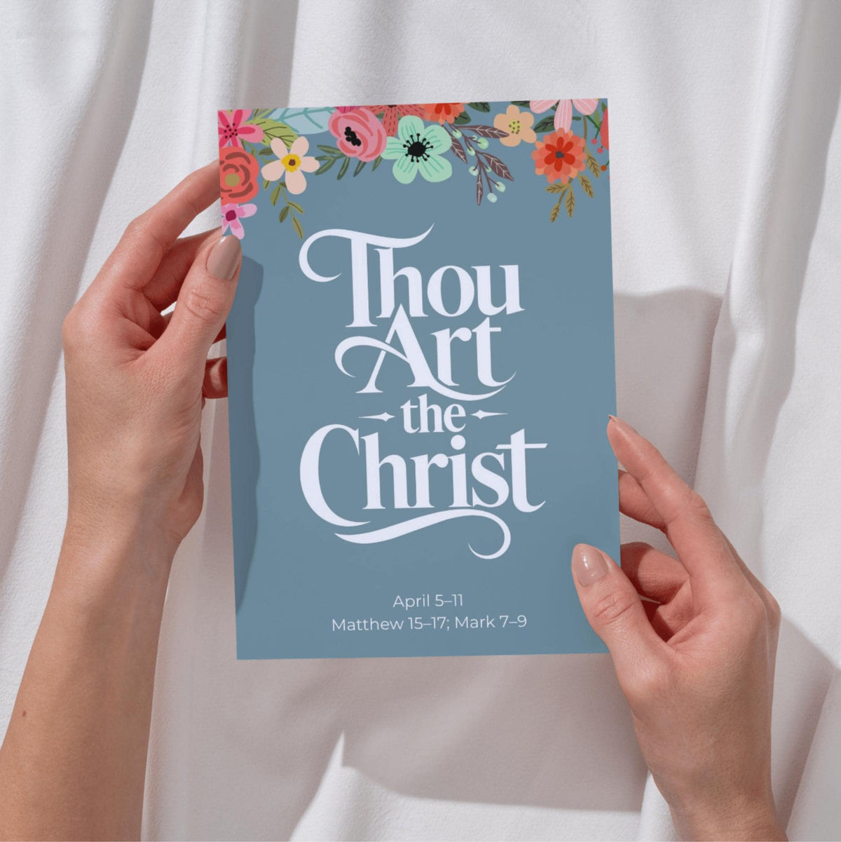 Hands holding a muted teal Thou Art the Christ printable New Testament scripture poster with flowers